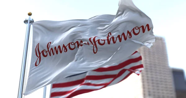 New Brunswick, NJ, ABD, 28 Ocak 2021: Johnson & Johnson logosu Amerikan bayrağıyla rüzgarda sallanıyor. Johnson & Johnson COVID-19 aşısının geliştirildiğini duyurdu