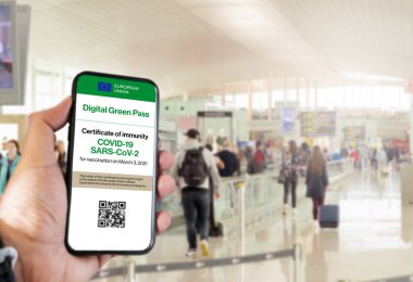 Avrupa Birliği 'nin QR kodlu dijital yeşil geçiş kartı arka planda bulanık havaalanı olan bir el tarafından tutulan bir cep telefonunun ekranında. Covid-19 'dan dokunulmazlık. Kısıtsız seyahat et.