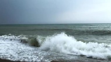 Kaba bir denizin köpüklü dalgaları bulutlu bir günde kıyıya vurdu..