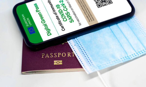 The digital green pass of the european union with the QR code on the screen of a mobile phone over a surgical mask and a passport. Immunity from Covid-19. Travel without restrictions.