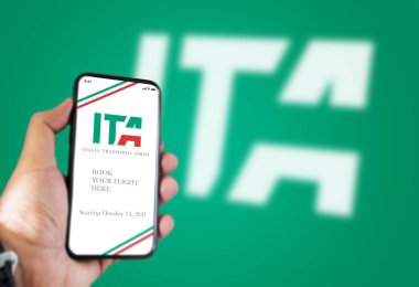 Roma, İtalya, Temmuz 2021: Ekranda ITA uygulaması ve yeşil bir fonda bulanık ITA logosu bulunan bir telefonu tutan el, 15 Ekim 2021 'den itibaren yeni İtalyan bayrak taşıyıcısı.