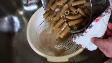 Pişirmek için kaynar suya çiğ makarnayı koymak. İtalyan yemeği. Çiğ tam teşekküllü rigatoni. Geleneksel İtalyan tarifine göre makarna pişirme