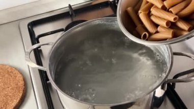 Pişirmek için kaynar suya çiğ makarnayı koymak. İtalyan yemeği. Çiğ tam teşekküllü rigatoni. Geleneksel İtalyan tarifine göre makarna pişirme