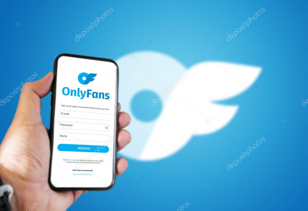 London, UK, August 2021; a hand holds a mobile phone with the OnlyFans registration form on the screen and the logo blurred in the background.