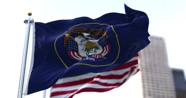アメリカのユタ州の旗がアメリカの星や縞模様の旗を背景に風に揺れる ユタ州は1896年に合衆国の第45代目として認められた 独立と団結 — ストック動画