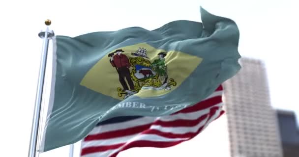 アメリカのデラウェア州の旗がアメリカの星や縞模様の旗を背景に風に揺れる 1787年12月7日 デラウェアはアメリカ合衆国初の州となった — ストック動画