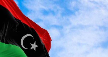 Açık bir günde Libya bayrağı sallanıyor. Kırmızı, siyah, yeşil çizgiler; beyaz yıldız ve siyah üzerine hilal. 3D illüstrasyon canlandırıcı. Dalgalanan kumaş. Seçici odaklanma. Sallanan bayrak