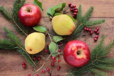 Doğal kırmızı elmalar, yapraklı sarı armutlar, kırmızı dikenli böğürtlenler, ve eski ahşap masada köknar dalları. Tahta arka plan ve taze organik meyveler. Sonbahar hasadı. Düz yatıyordu. Kırsal biçim