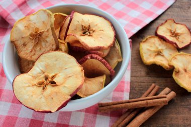 Kurutulmuş elma halkaları bir kasede ve tarçın çubukları ahşap arka planda. Üst Manzara. Kırsal biçim