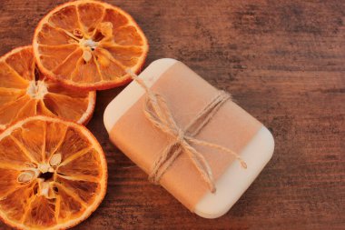 Kağıda sarılmış turuncu sabun çubuğu ve ahşap masada kurutulmuş portakal dilimleri. El yapımı vücut bakım ürünleri. Üst görünüm, alanı kopyala