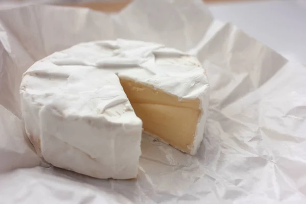 Camembert cheese on white packaging paper. Top view. Close up of white cheese