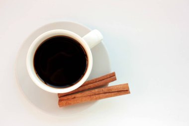 Beyaz arka planda tarçın çubukları olan bir fincan kahve. Üst görünüm, alanı kopyala