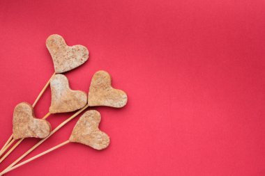 Kırmızı arka planda çubuk üzerinde kalp şeklinde kurabiyeler. Sevgililer Günü hediyeleri renkli arka planda. Düz yat, boşluğu kopyala