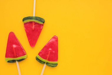 Sarı arkaplanda karpuz dondurması. Parlak yaz geçmişi. Karpuz şeklinde lolipop. Çubukta şeker. Üst görünüm, alanı kopyala