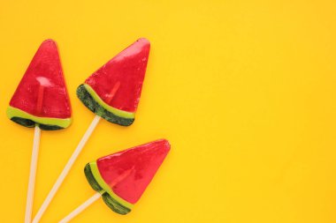 Sarı arkaplanda karpuz dondurması. Parlak yaz geçmişi. Karpuz şeklinde lolipop. Çubukta şeker. Üst görünüm, alanı kopyala