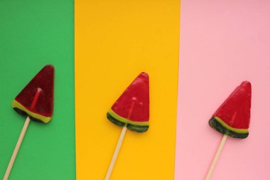 Renkli arka planda karpuz dondurması. Parlak yaz geçmişi. Karpuz şeklinde lolipop. Çubukta şeker. Üst görünüm, alanı kopyala