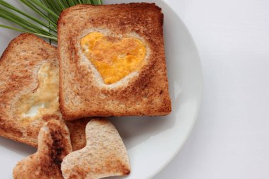 Kalp şeklinde bir delikte kızarmış yumurtalı tost ekmeği ve beyaz arka planda yeşil tabaklar. Yaratıcı Sevgililer Günü ya da Anneler Günü kahvaltı fikri