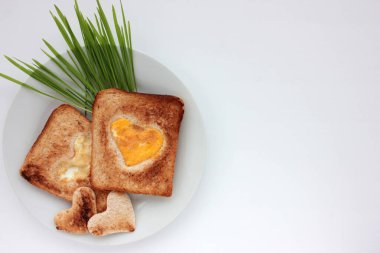 Kalp şeklinde bir delikte kızarmış yumurtalı tost ekmeği ve beyaz arka planda yeşil tabaklar. Yaratıcı Sevgililer Günü ya da Anneler Günü kahvaltı fikri