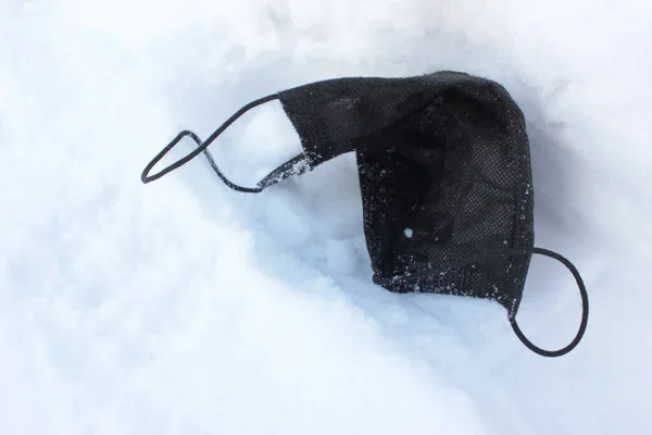 コロナウイルスのパンデミックの間 冬の通りの黒い薬用顔のマスクを廃棄しました 雪の背景に外科用マスクを使用しました スペースのコピー — ストック写真