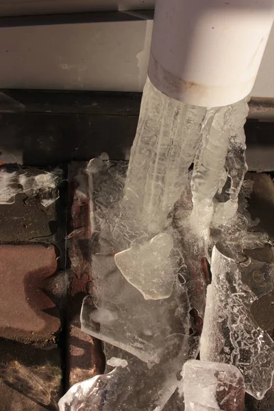 在白色塑料雨水管中的冻水 铺石板背景上破碎的冰柱 — 图库照片