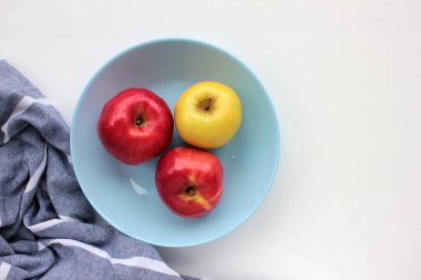 Mavi tabakta kırmızı ve yeşil elma. Taze meyve manzarası ve beyaz masa arkasında çizgili gri peçete. Boşluğu kopyala