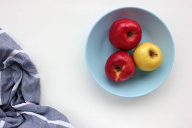 Mavi tabakta kırmızı ve yeşil elma. Taze meyve manzarası ve beyaz masa arkasında çizgili gri peçete. Boşluğu kopyala