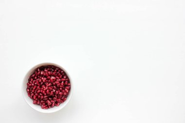 Beyaz masa arkasındaki bir kasede kırmızı nar tohumları. Düz besin kompozisyonu. Üst görünüm, alanı kopyala. 