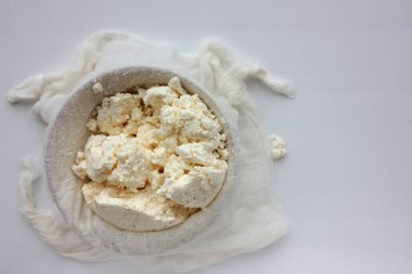 Beyaz masa arkaplanındaki kâsede taze yapılmış yumuşak süzme peynirin yakın plan çekimi. Peynir bezinden ev yapımı ricotta. Üst görünüm