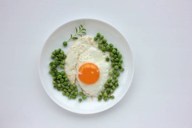 Beyaz masa arkasında yeşil bezelyeli sahanda yumurta. Sağlıklı kahvaltı ya da brunch konsepti. Sunny Side ve sebzeler bir tabakta servis edilir. Üst görünüm