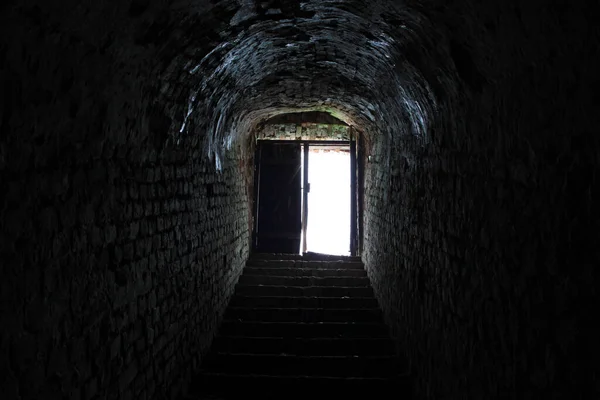 Light in the end of dark tunnel. Brick walls and concrete stairs to the light from the dungeon
