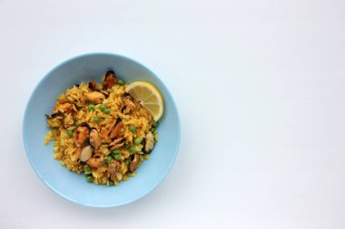 Geleneksel İspanyol deniz ürünleri yemeği paella ve limon dilimi. Beyaz arka planda mavi tabakta yeşil bezelyeli risotto. Üst görünüm, boşluğu kopyala. Sağlıklı yeme kavramı