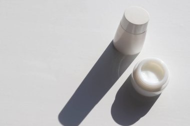 Cam kavanozda yüz kremi ve beyaz masa arkasında bir şişe losyon. Sert ışık, gölge. Cilt ve vücut bakımı için doğal güzellik ürünleri. Yaz yaşam tarzı. Üst görünüm, alanı kopyala