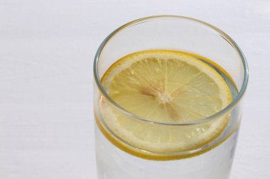 Beyaz masa arka planında limon dilimi olan yakın plan bir bardak su. Üst görünüm, boşluğu kopyala. Yaz ferahlatıcı soğuk içecek.