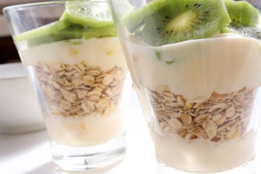 Sağlıklı kahvaltı yoğurdu, yulaf ezmesi ve beyaz masa arkasında gözlüklü kivi. Üst görünüm