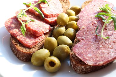 Çavdar ekmekli sandviç üzerine salamlı pepperoni ve beyaz masa arkasında yeşil zeytin turşusu. Düz yerde yemek vardı. Üst görünüm, boşluğu kopyala. Seçici odak