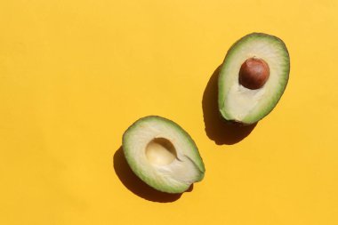 Avokado sarı arka planda ikiye bölündü. Üst görünüm, boşluğu kopyala. Sert ışık, gölge