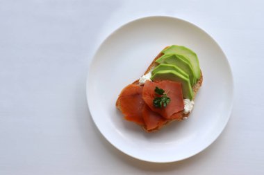 Tütsülenmiş somon, avokado, krem peynir ve maydanozlu beyaz ekmek. Beyaz arka planda kahvaltıda sağlıklı tost tabağı. Üst görünüm, alanı kopyala