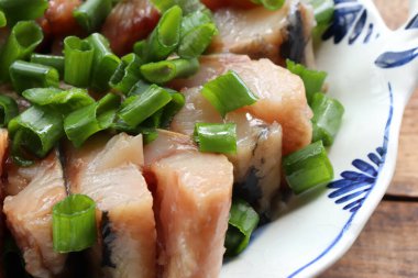 Yeşil soğan ve limon dilimli bir tabakta tuzlanmış ringa balığı parçaları. Ahşap masa arkasında İsveç usulü ringa balığı turşusu. Yaz ortası geleneksel yemekleri. Üst görünüm, alanı kopyala