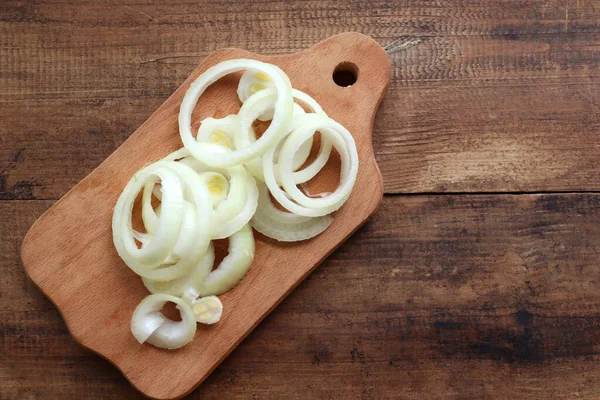Raw onion rings on wood cutting board on wooden background. Top view, copy space