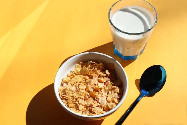 Bowl of cereal and glass of milk on yellow background. Healthy breakfast with cornflakes and milk. Top view, copy space. Hard light, shadow