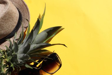 Sarı zemin üzerinde ananas, güneş şapkası ve güneş gözlüğü olan düz bir kompozisyon. Üst görünüm, boşluğu kopyala. Sert ışık, gölge