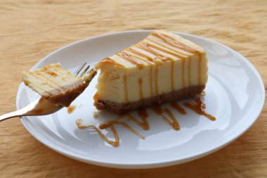 New York 'tan bir parça peynirli kek. Masa örtüsünün üzerinde çatal ve tabak üzerine karamel sosu. Peynirli keke yakın çekim. Üst görünüm