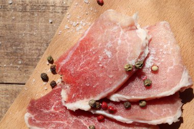 Kesme tahtasında çiğ domuz pirzolası. Baharat, biber, tuz ve ahşap zemin üzerinde pişmemiş et biftekleri. Üst görünüm 