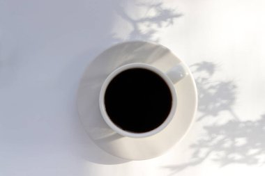 Arka planda çiçek gölgesi olan beyaz bir masada bir fincan kahve. Bahar ya da yaz düzlüklerinde hayat vardı. Üst görünüm, alanı kopyala