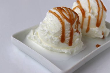 Beyaz masa arkaplanında karamelli vanilyalı dondurma kepçeleri. Karamel şuruplu donmuş yoğurt. Yaz tazeleyici tatlı. Üst görünüm