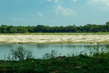 Küçük bir nehrin her iki yakasında yeşil çimenler ve beyaz bir bulut ve mavi bir gökyüzü.