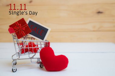 Çin 'de online alışveriş, 11.11 single' ın günlük satış konsepti. Alışveriş arabası ve kırmızı kalp yastığı beyaz ve kahverengi arka planda. 11.11 nolu metin için fotokopi alanı var..