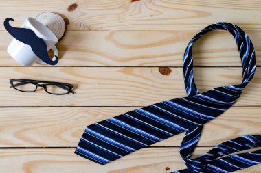 Arka plan bulanıklığı, Babalar Günü konsepti. Siyah bir bıyık kağıdı, mavi bir kravat, mavi bir hediye kutusu ve tahta masada gözlük..