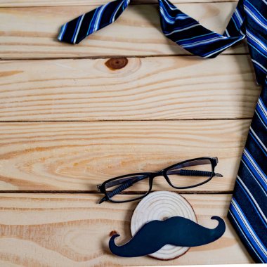 Babalar günün kutlu olsun. Siyah bir bıyık kağıdı, mavi bir kravat, mavi bir hediye kutusu ve tahta masada gözlük..