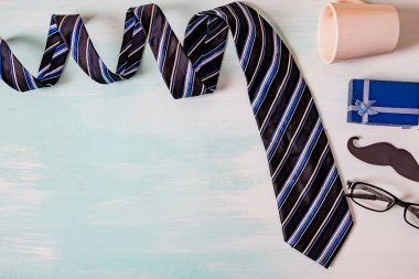 Babalar günün kutlu olsun. Siyah bir bıyık kağıdı, mavi bir kravat, mavi bir hediye kutusu ve tahta masada gözlük..